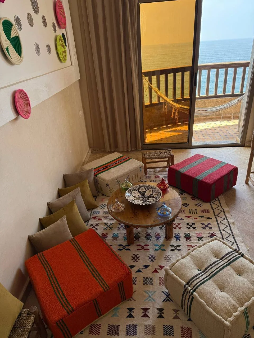 Living room with colorful furniture and a view of the ocean through a sliding glass door.