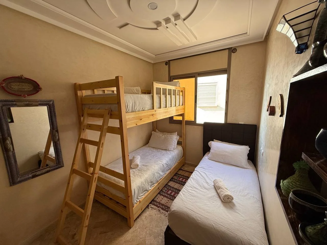 Small bedroom with a wooden bunk bed, a single bed, a window, a mirror, and wall decorations.