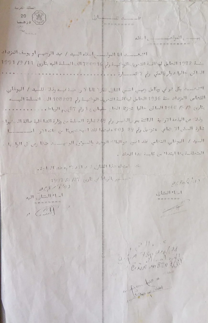 A wrinkled official document written in Arabic, with signatures and a stamp at the top, on a white sheet of paper.