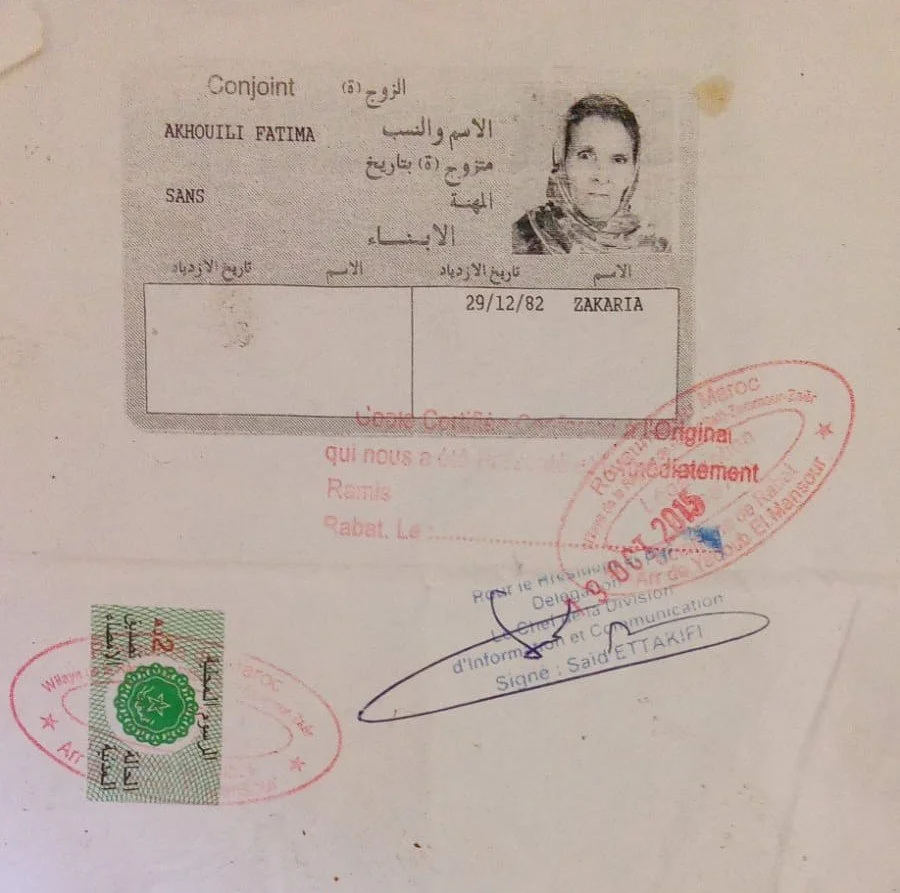 A scanned document with Arabic and French text, containing a black and white photo of a woman in the top right corner, various stamps including red and green, and handwritten notes.