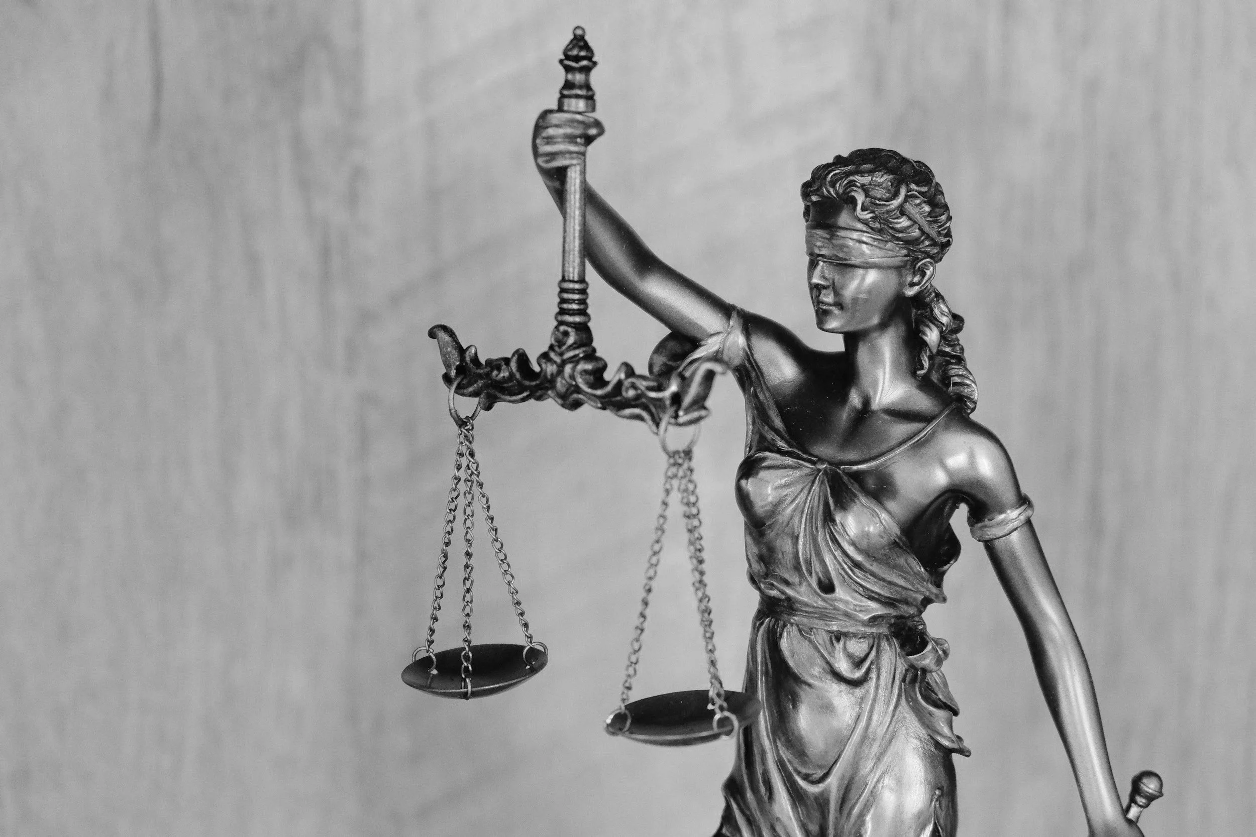 Adalet denge ölçüsü tutan kadın figürü, elinde tartı tutuyor, arka plan gri ve sade.