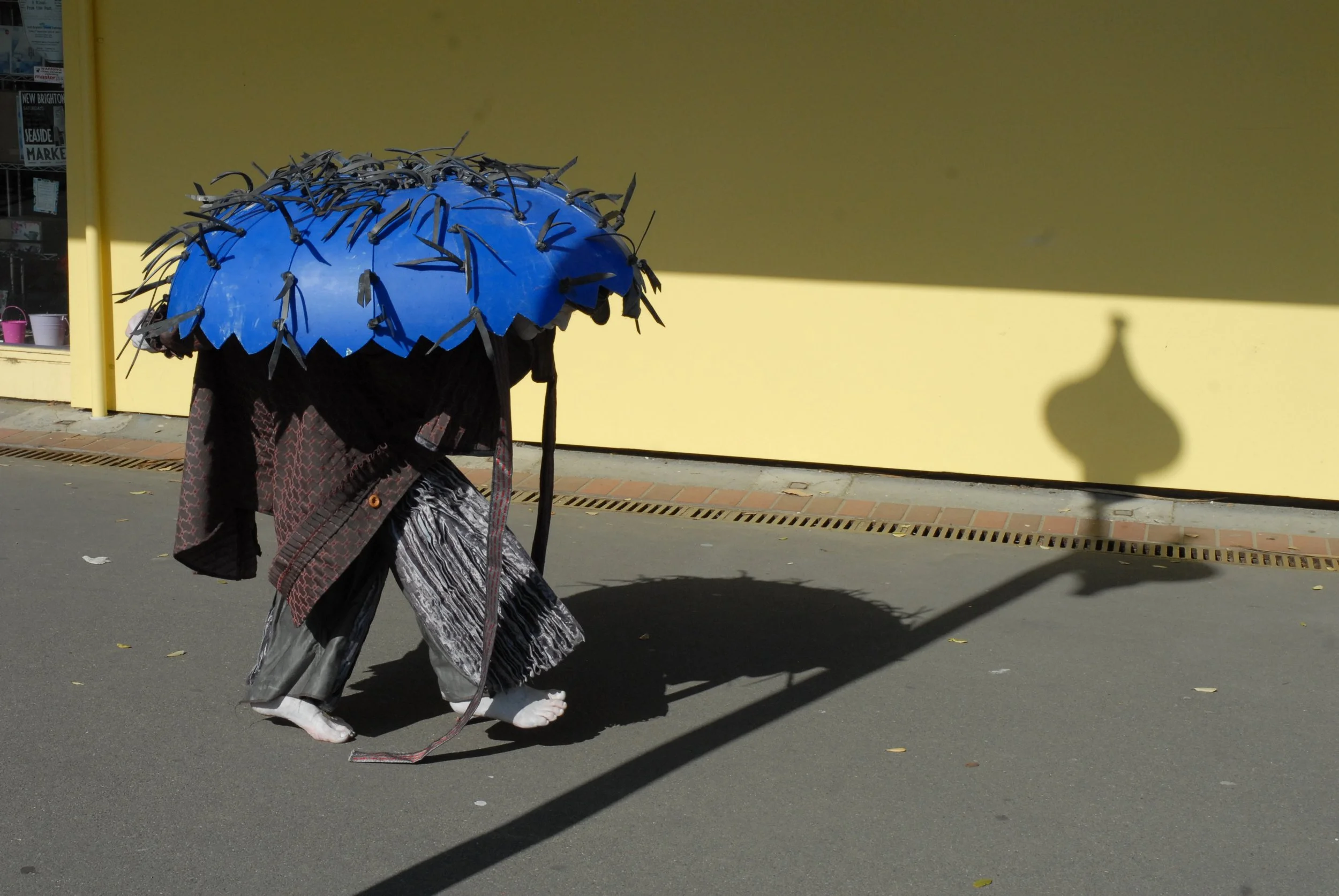 Performer on an empty street wearing a coat and large blue head sheild