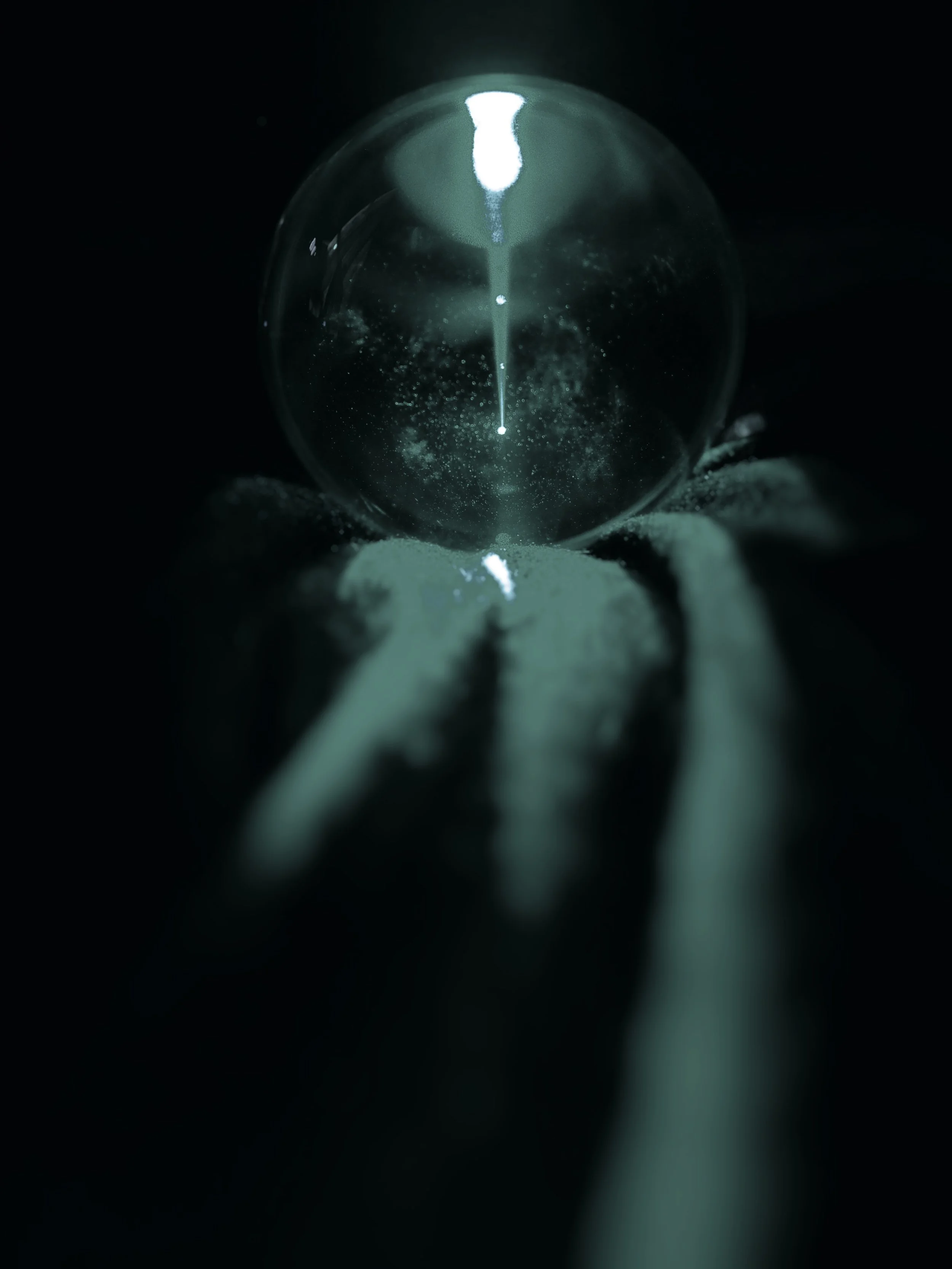 Close-up of a glass sphere with a reflective surface, placed on a surface with a blurred, dark background