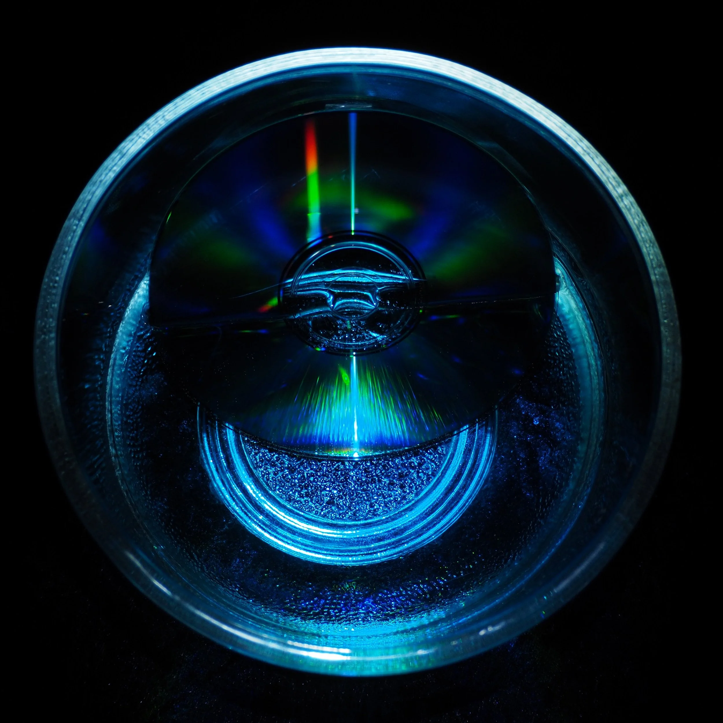 Close-up of a glass lens reflecting green, red, and blue laser light against a black background.