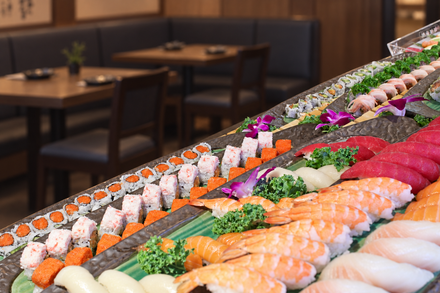 Assorted sushi platter with various types of sushi, garnished with purple orchids and green leafy decorations, on a green platter in a restaurant setting.