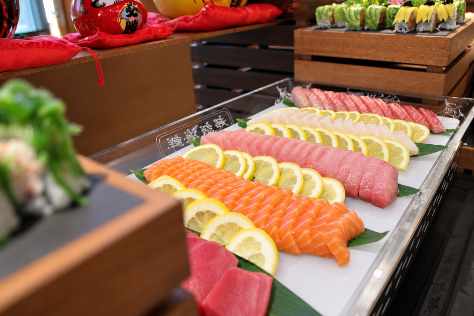 Assorted slices of raw fish, including salmon, tuna, white fish, and yellowtail, arranged on a platter with lemon slices and green leaves for garnish.