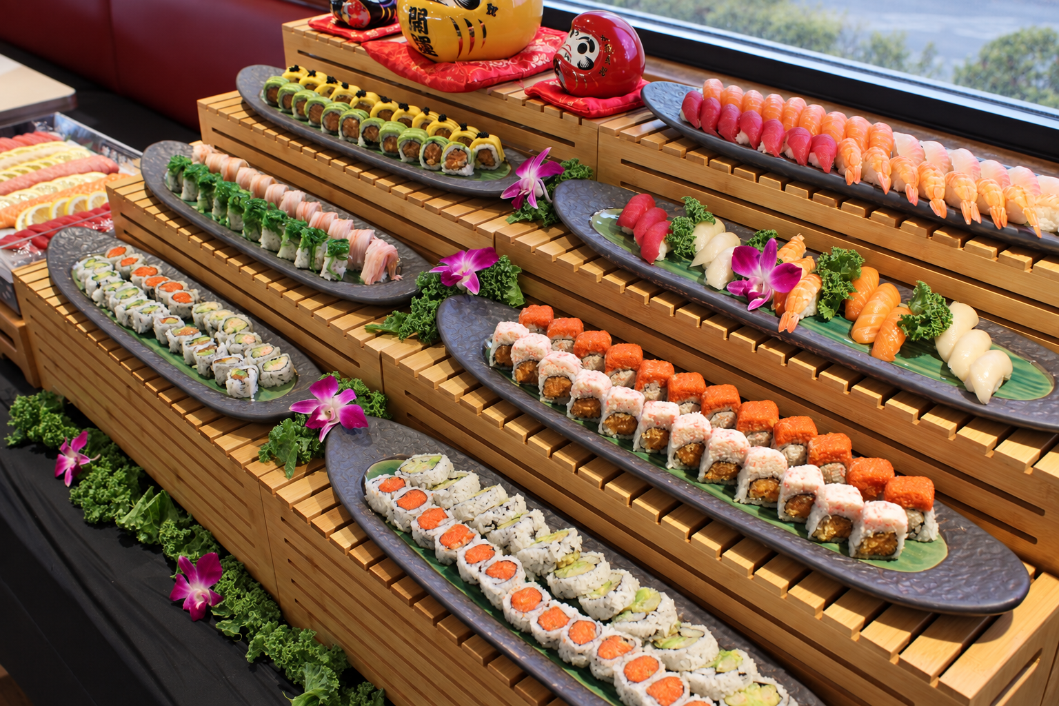 Sushi platter with various types of sushi arranged on black elongated plates decorated with purple orchids, green lettuce, and sushi dolls, set on wooden pedestals near a window with a city landscape in the background.