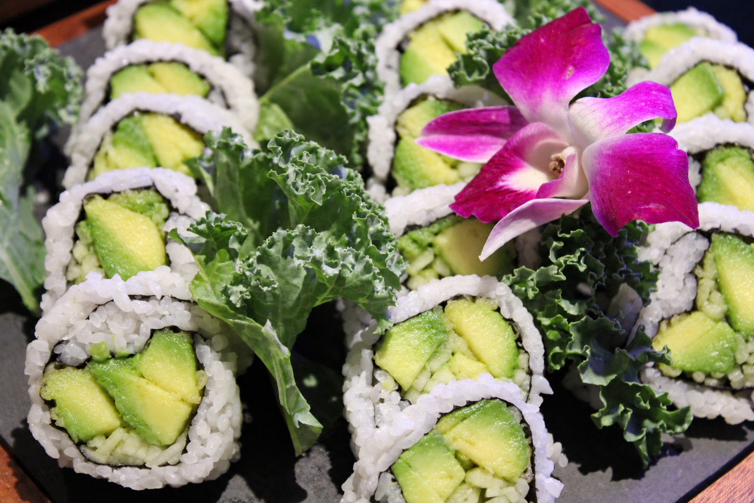 Sushi rolls filled with avocado and rice, garnished with kale and a pink orchid flower.