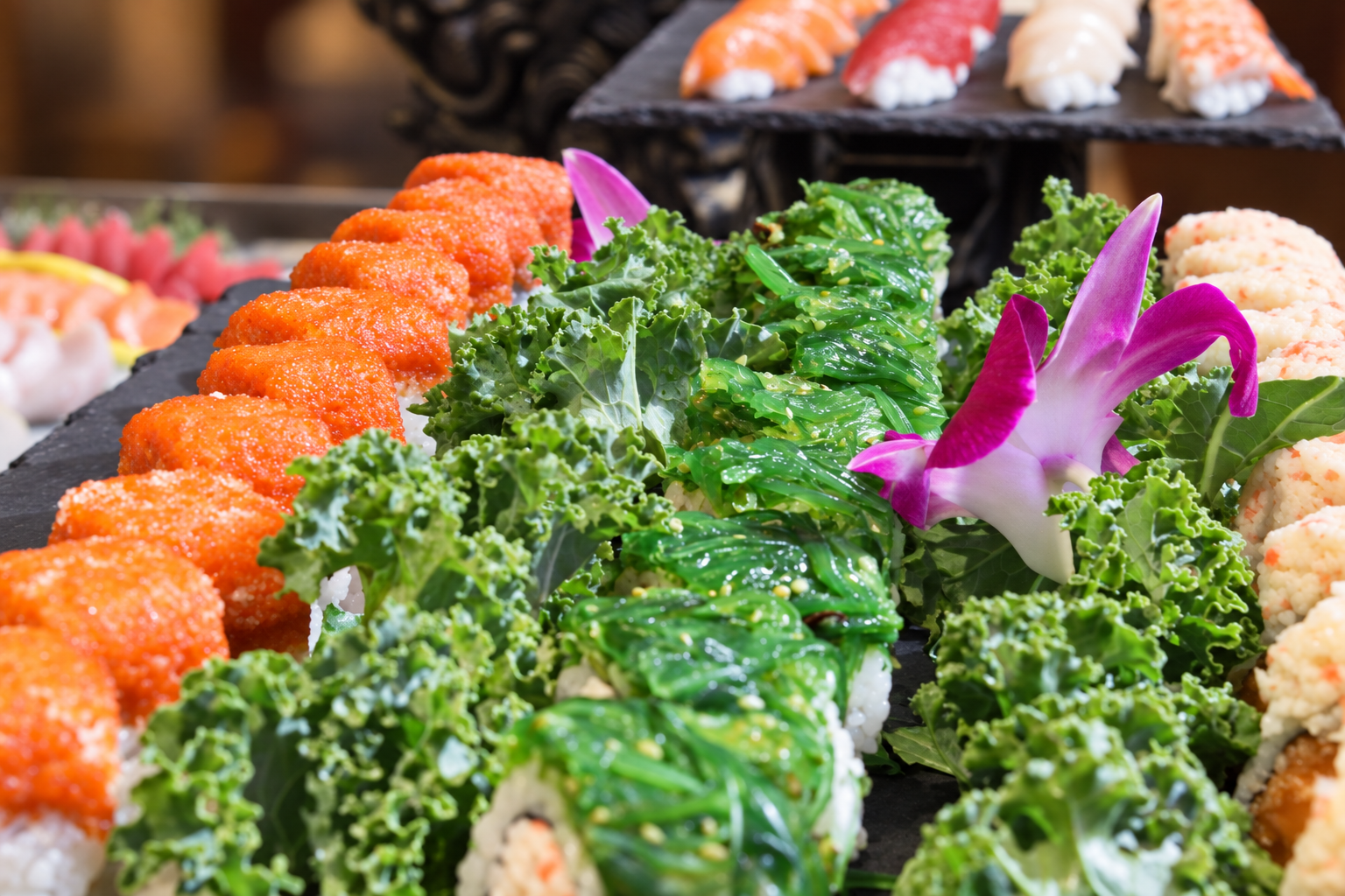 Various sushi rolls garnished with greens and flowers displayed on a black tray.