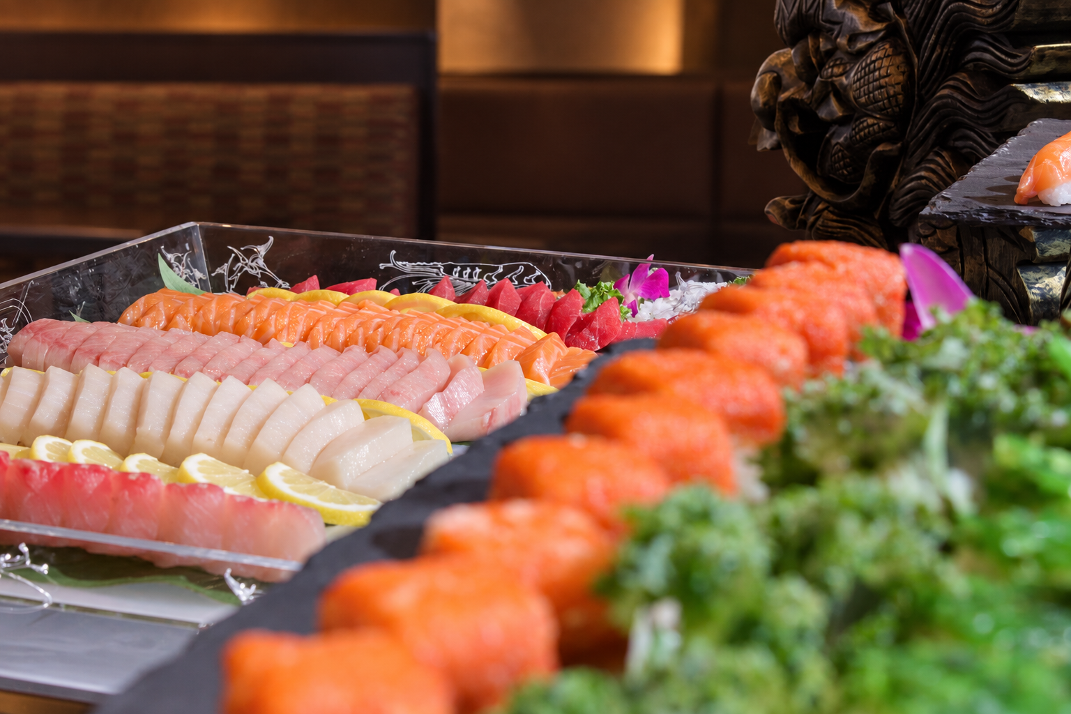 Assorted sashimi slices including tuna, salmon, white fish, and shrimp, garnished with lemon slices, arranged on a platter at a sushi restaurant.