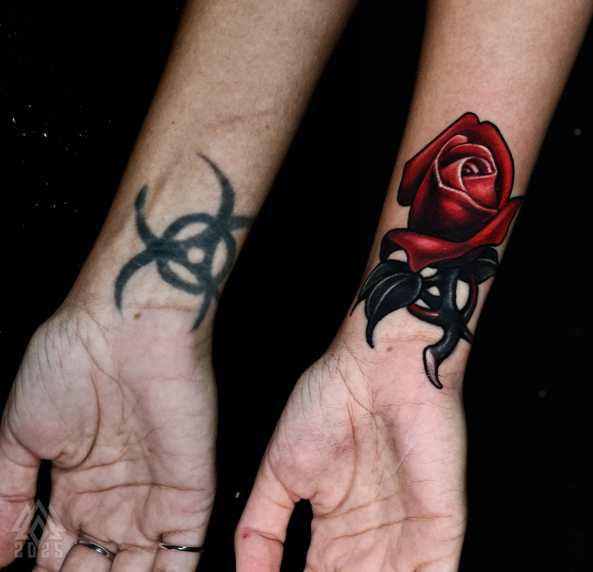 Cover-up tattoo before and after: a faded black tribal biohazard symbol on the wrist covered with a red rose and dark thorned stem, tattooed by Javi Antunez at Tattooed Theory in Mooresville, NC.