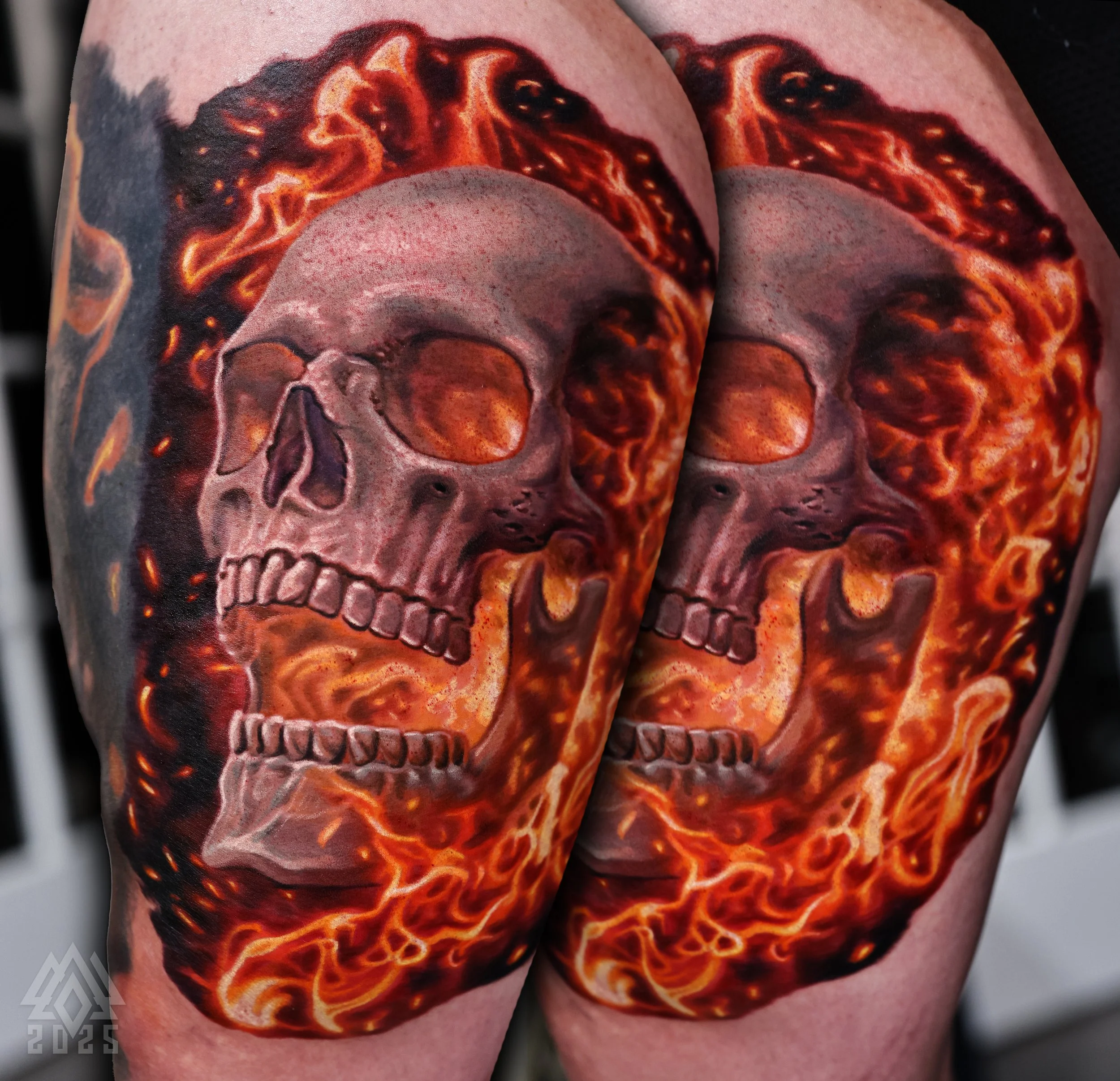 Tattoo of a realistic human skull with fiery orange and red flames around it.