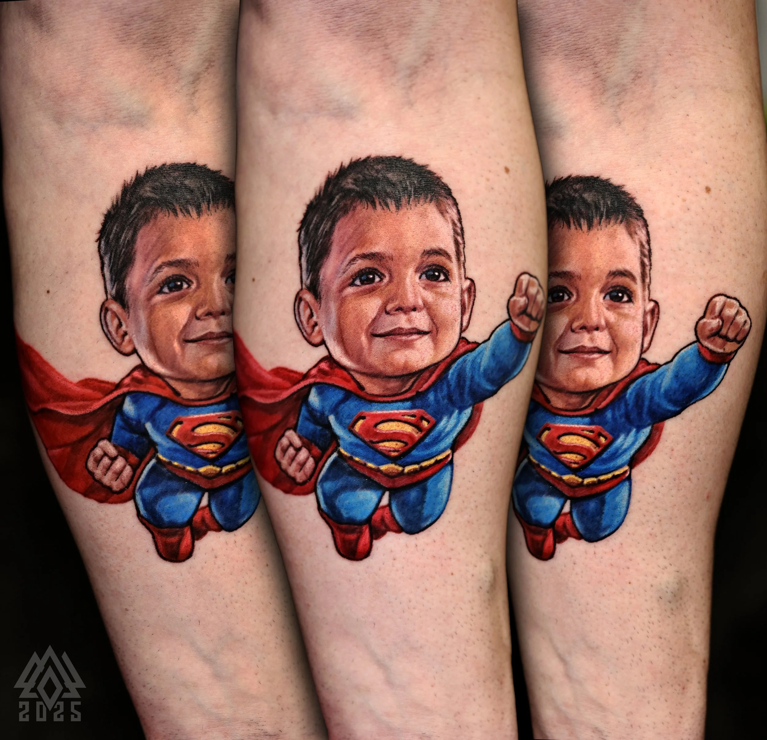 Tattoo of a smiling boy with short dark hair, wearing a red and blue superhero costume with a Superman logo, on a person's arm.