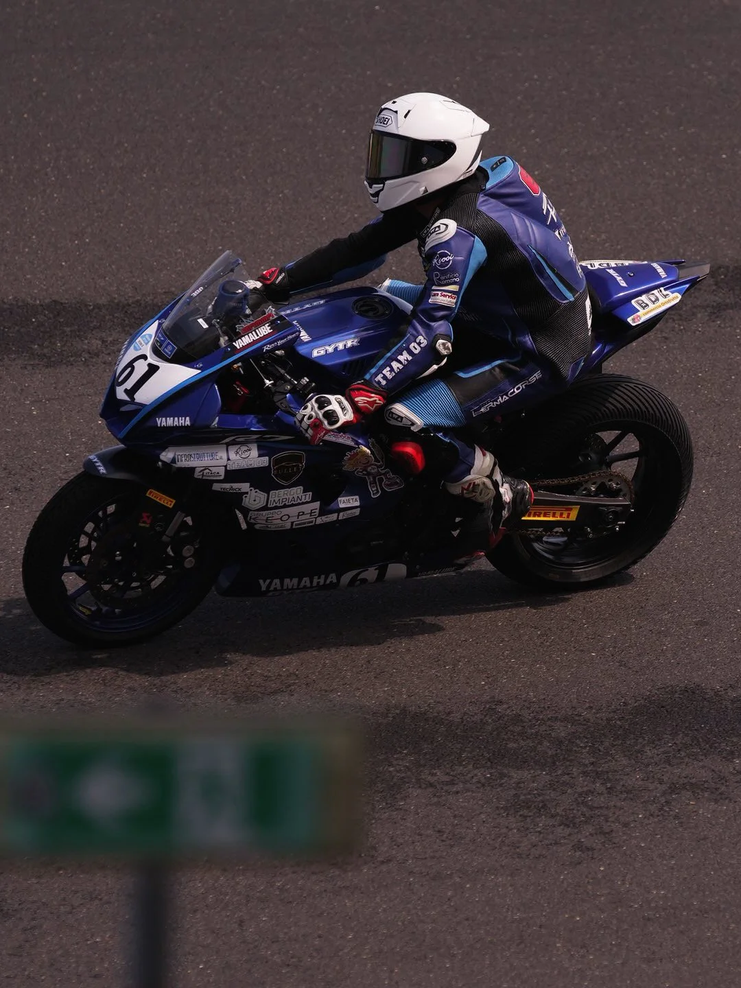 A motorcycle racer in a blue and black racing suit and white helmet riding a blue Yamaha sportbike on a paved track.