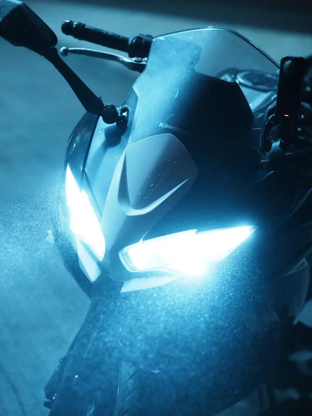 Close-up of a motorcycle with bright headlights on, showing the handlebars, windshield, and front bodywork.