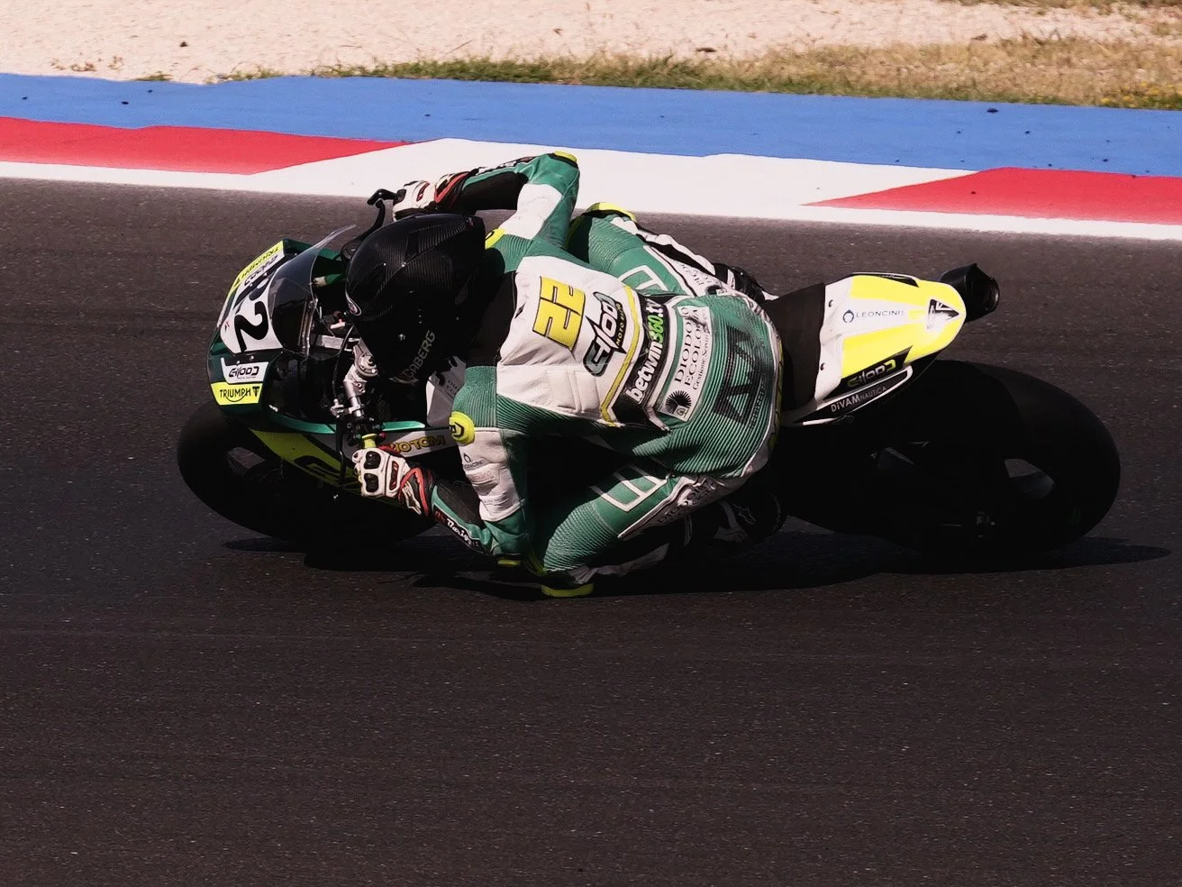 Motorcycle racer leaning into a turn on a race track, wearing a green and white suit and black helmet.