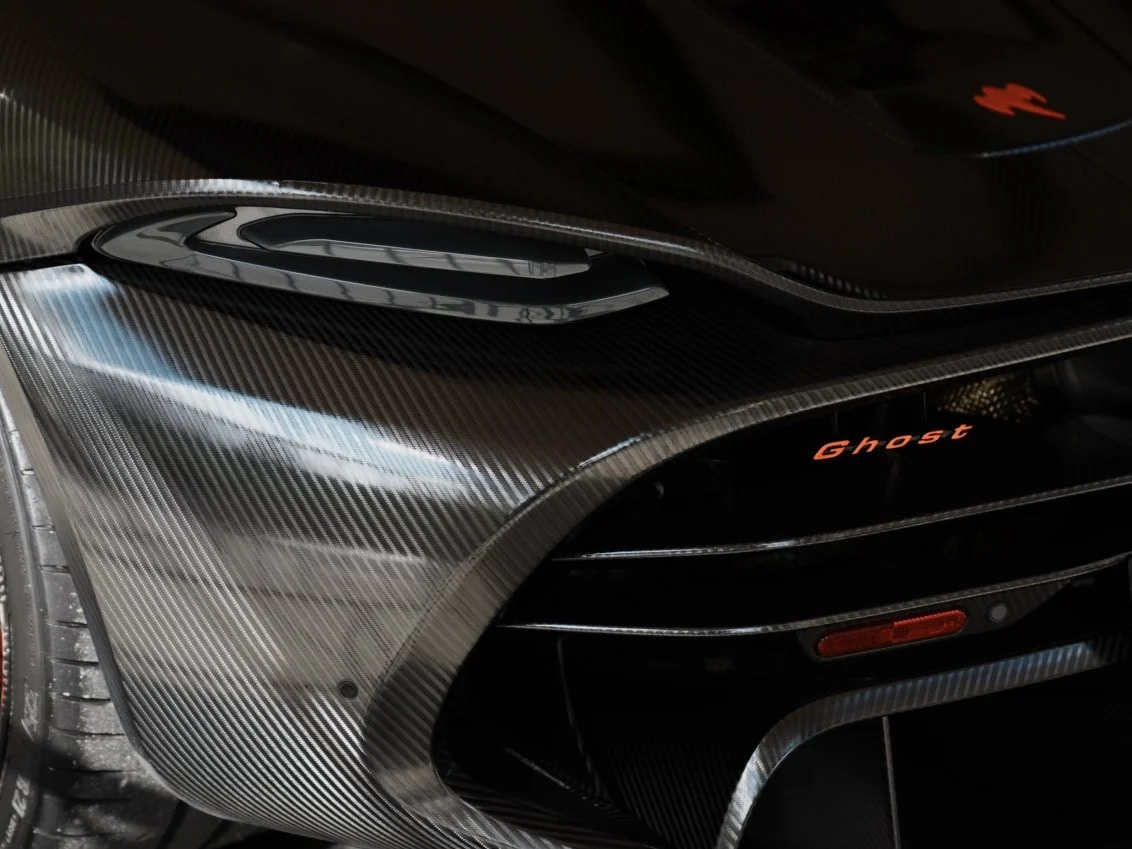 Close-up of a high-performance car hood made of carbon fiber with air vents, with the word 'Ghost' illuminated on the front grille area.