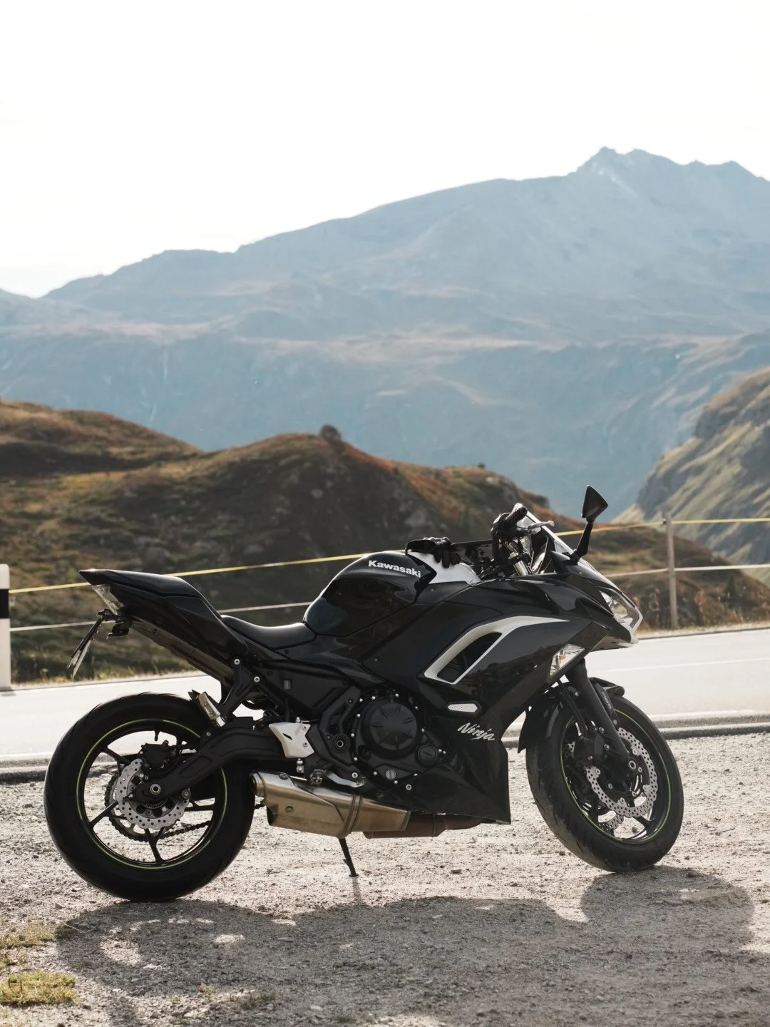 A black Kawasaki Ninja sport motorcycle parked on the side of a mountain road with mountains in the background.