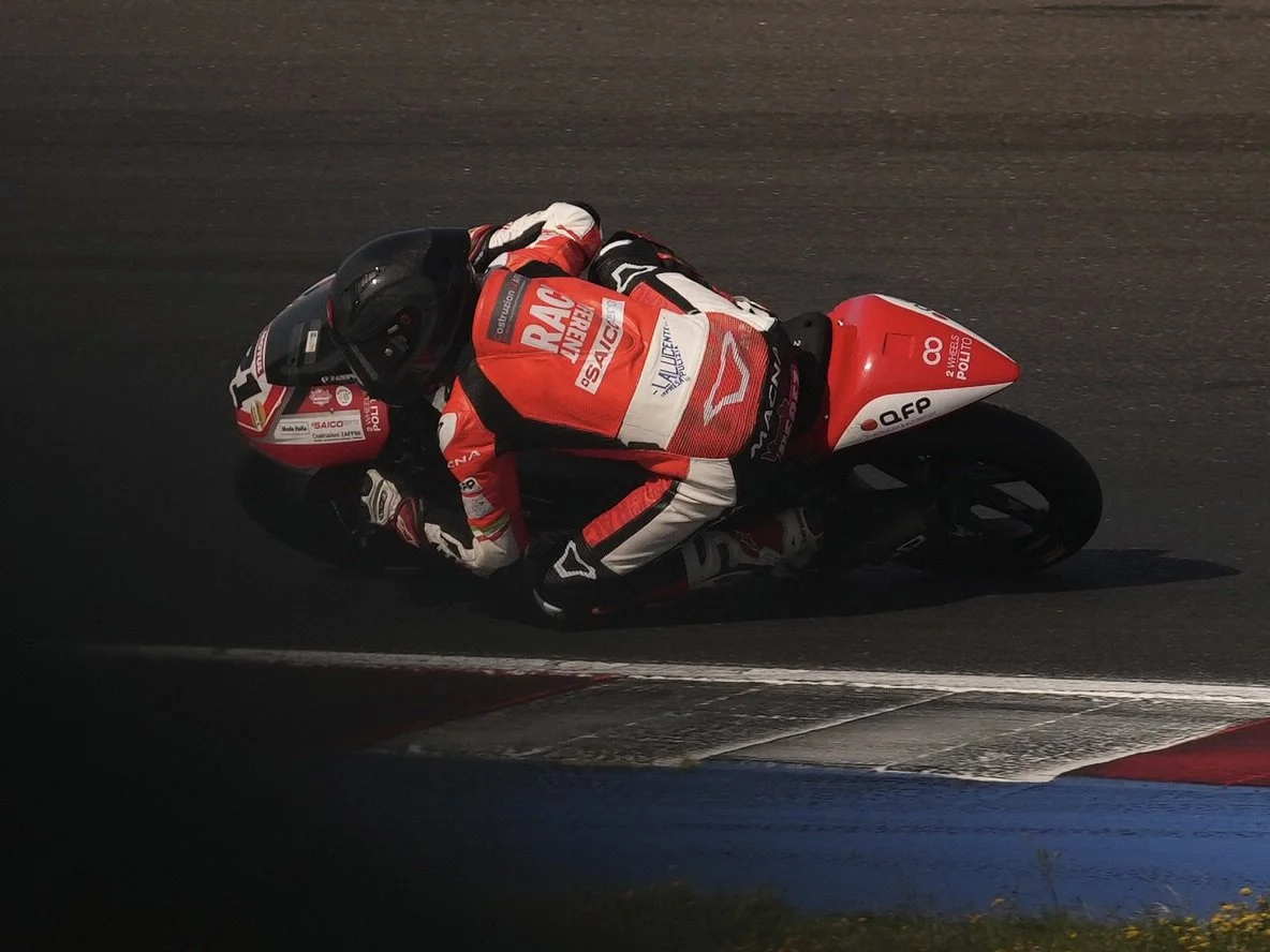 Motorcycle racer in red and white racing gear leaning into a turn on a race track at night.