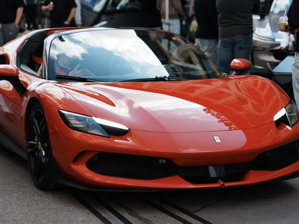 Red Ferrari sports car on display at a car show, with people in the background.