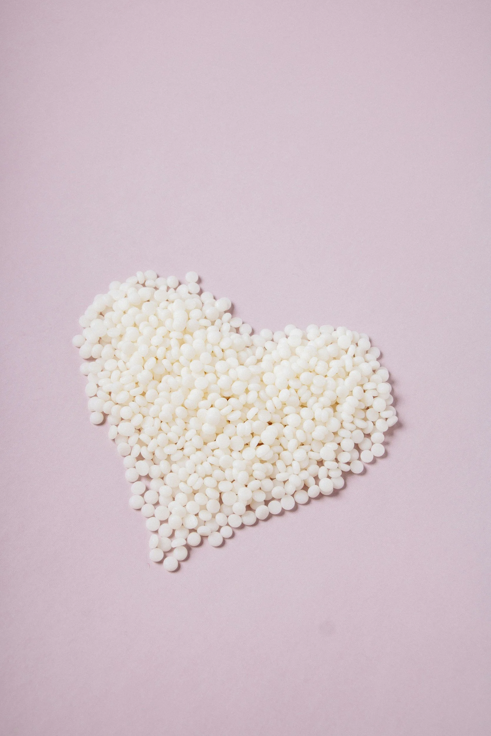 White wax beads arranged in a heart shape on a pink background.