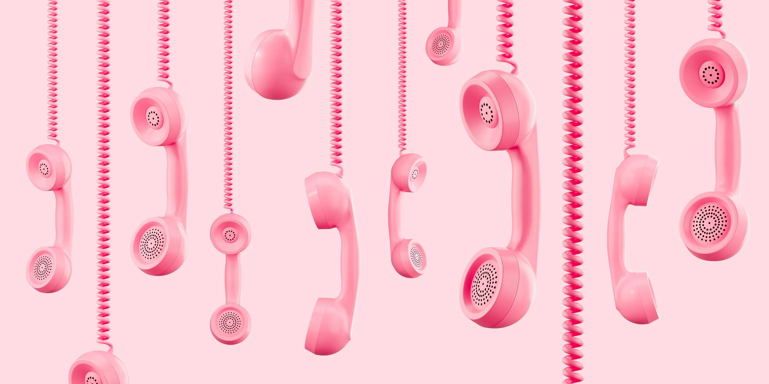 Pink telephone handsets hanging by their coiled cords against a pink background.
