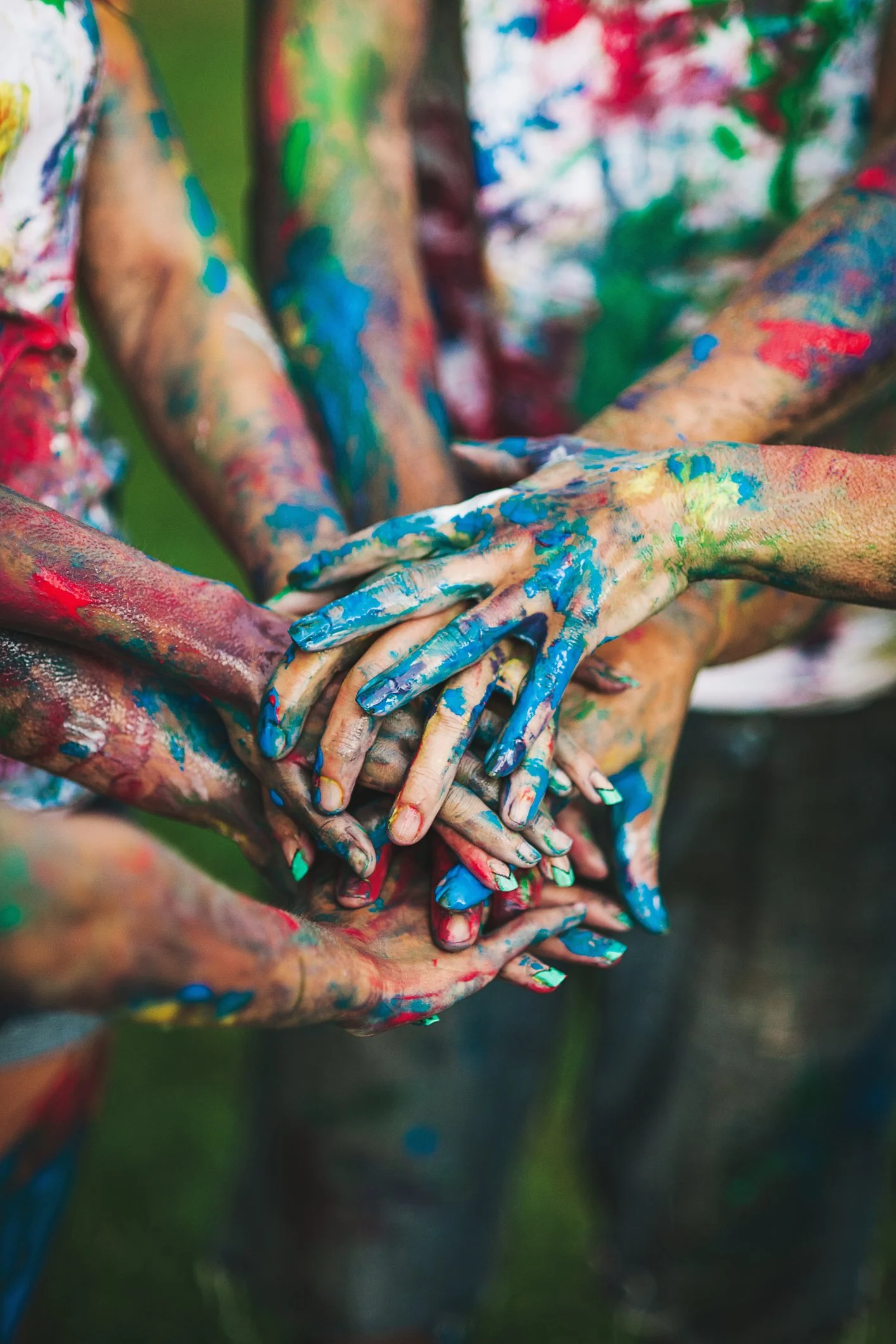 Several hands covered in colorful paint, stacked together.