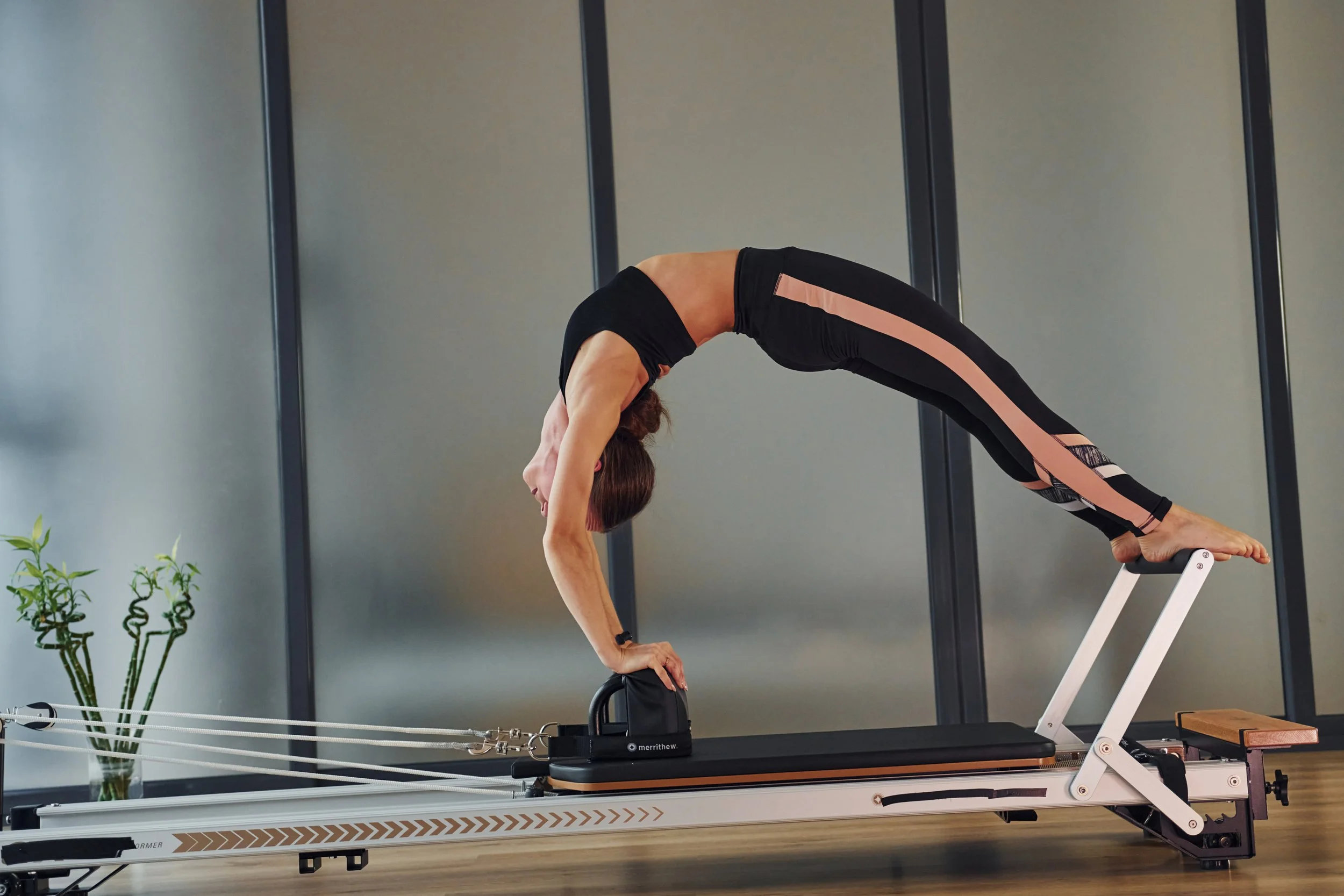 Woman performing yoga pose on Pilates reformer machine in home gym.
