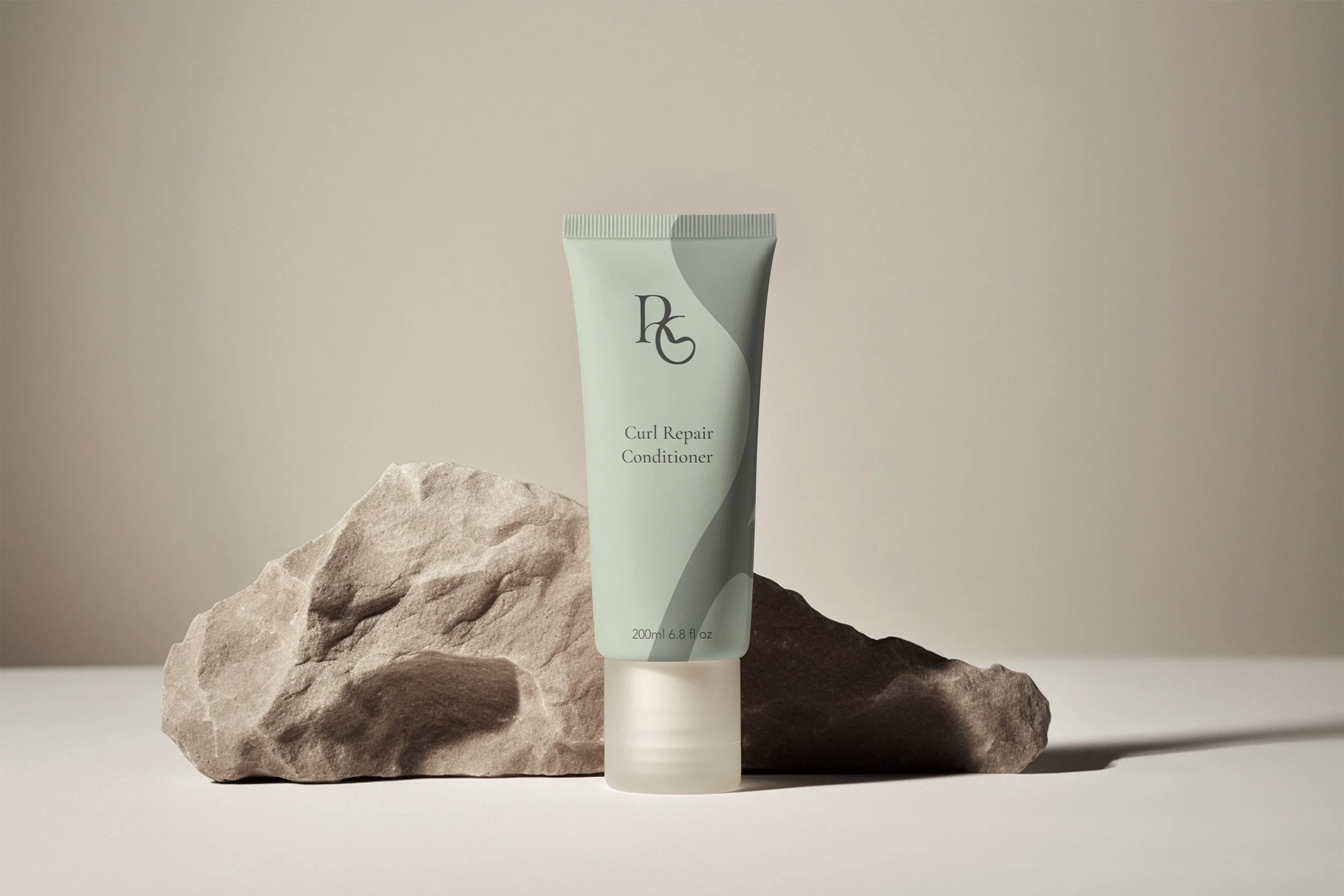 A tube of curl repair conditioner standing upright on a white surface, with a large rock behind it.
