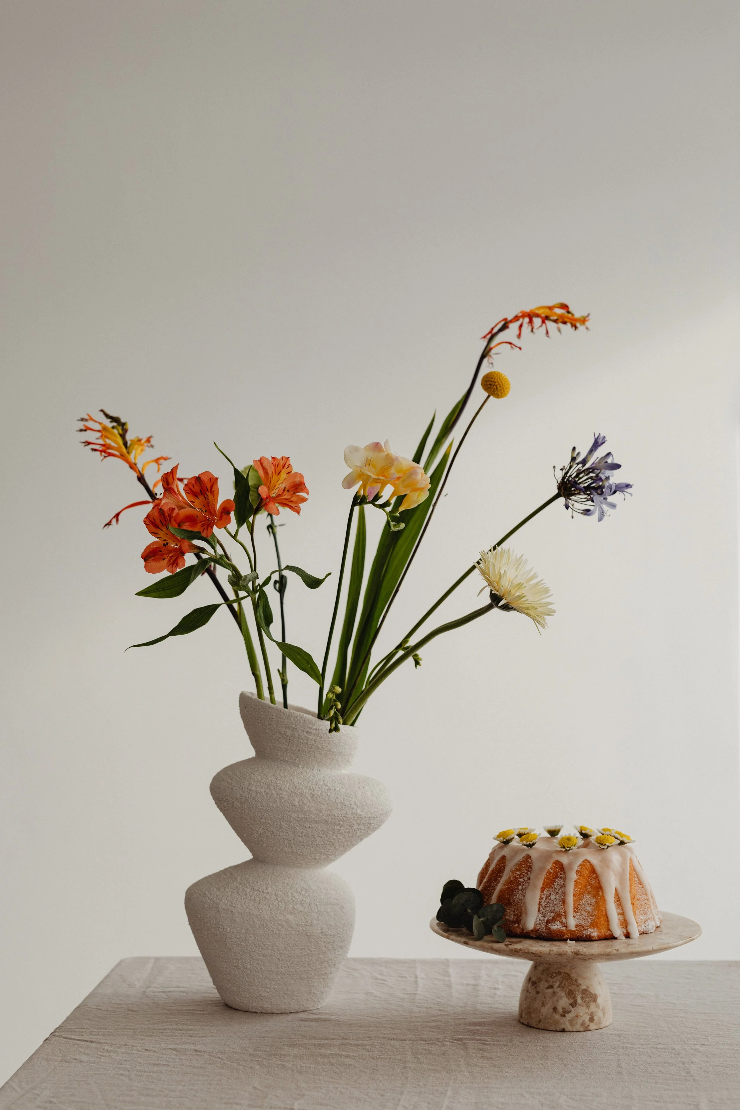 Modern white vase with colourful flowers next to a decorated cake