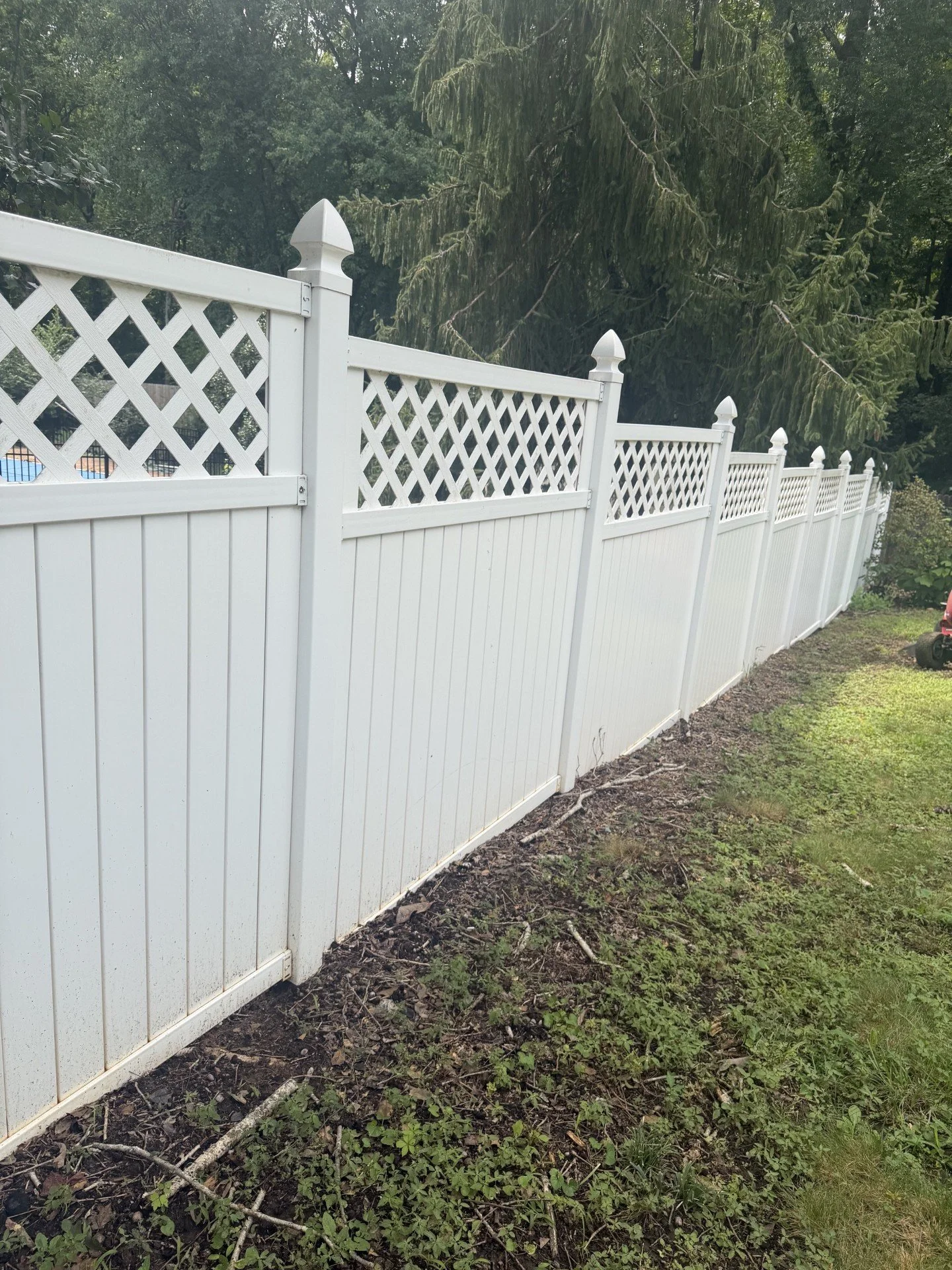White vinyl privacy fence with decorative lattice top in a backyard with green grass and trees.