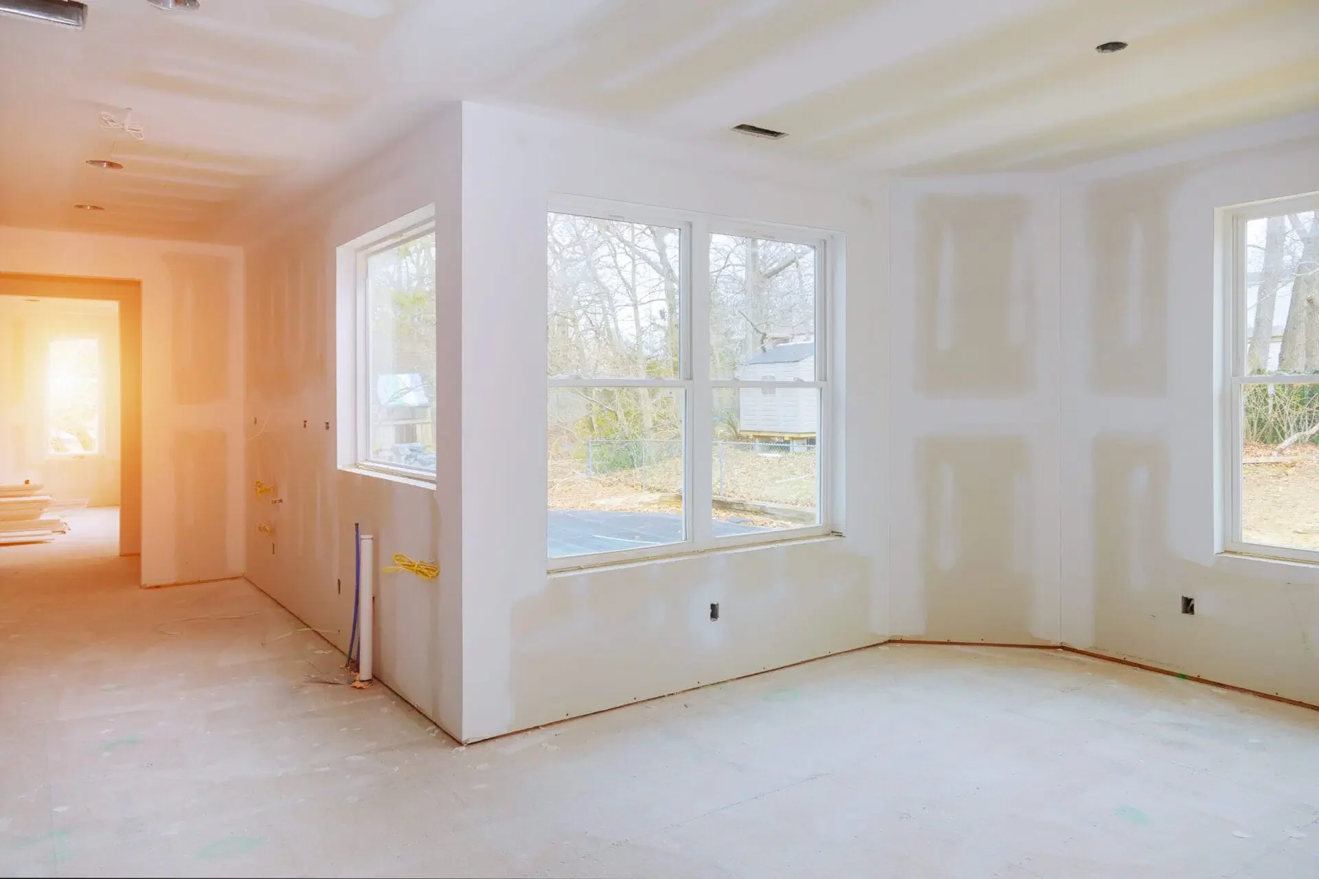 Interior of a house under construction with unfinished white walls, large windows, and exposed electrical wiring.