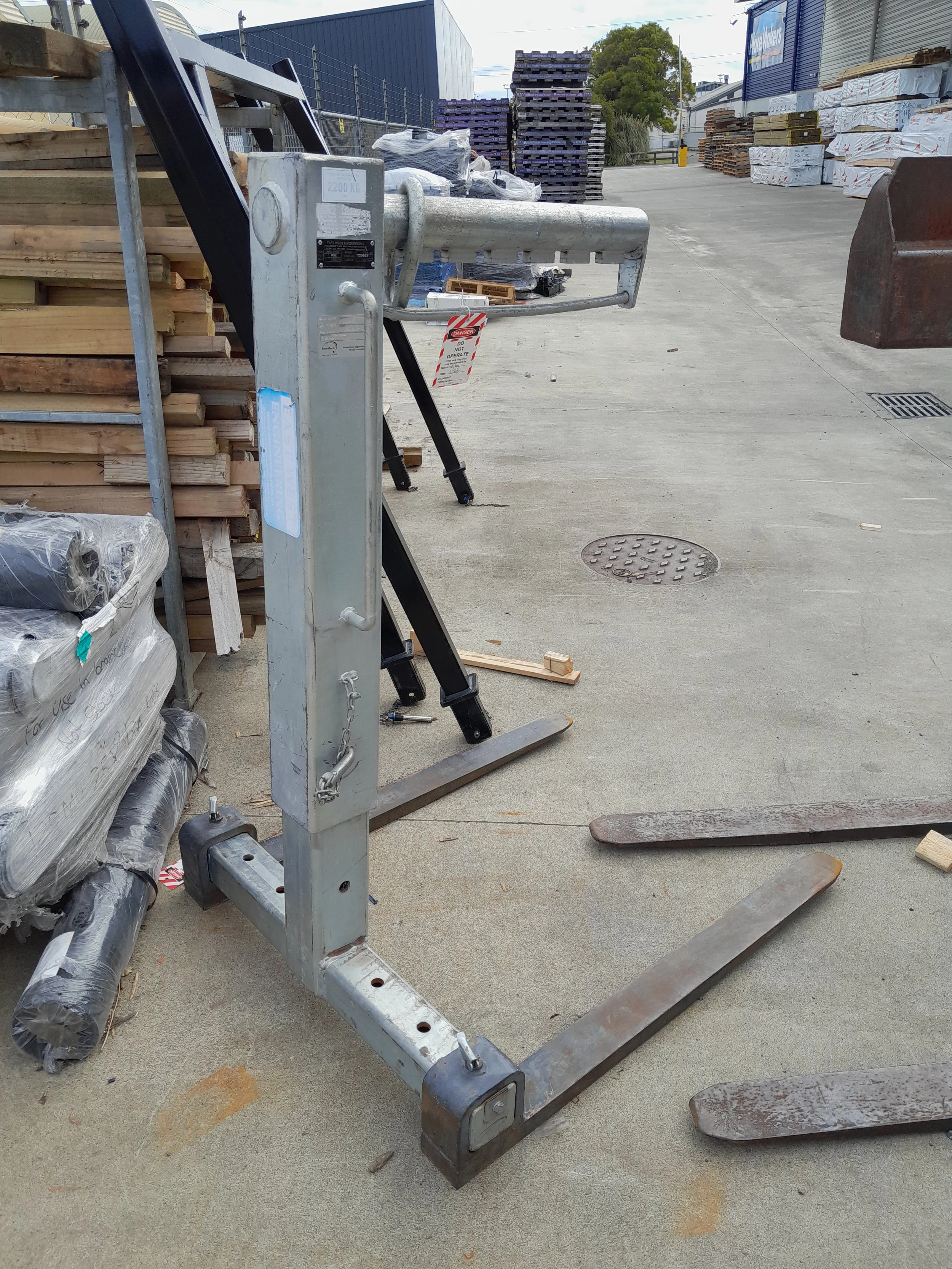 A grocery cart forklift attachment in an outdoor industrial area, surrounded by pallets, boxed items, and construction materials.
