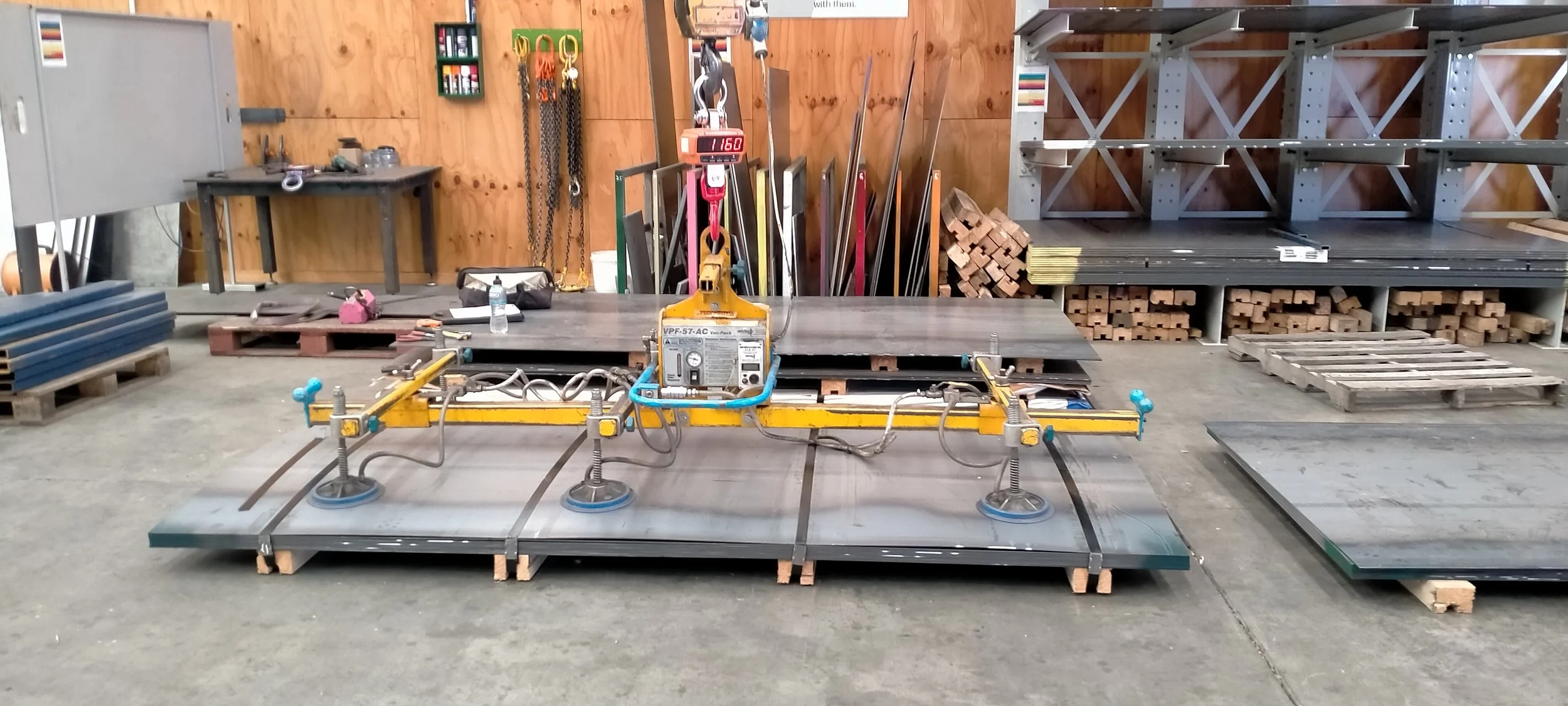 A workshop with a laser level and measurement tools set on a metal table, surrounded by wooden and metal materials, with storage shelves and tools hanging on the wooden walls.