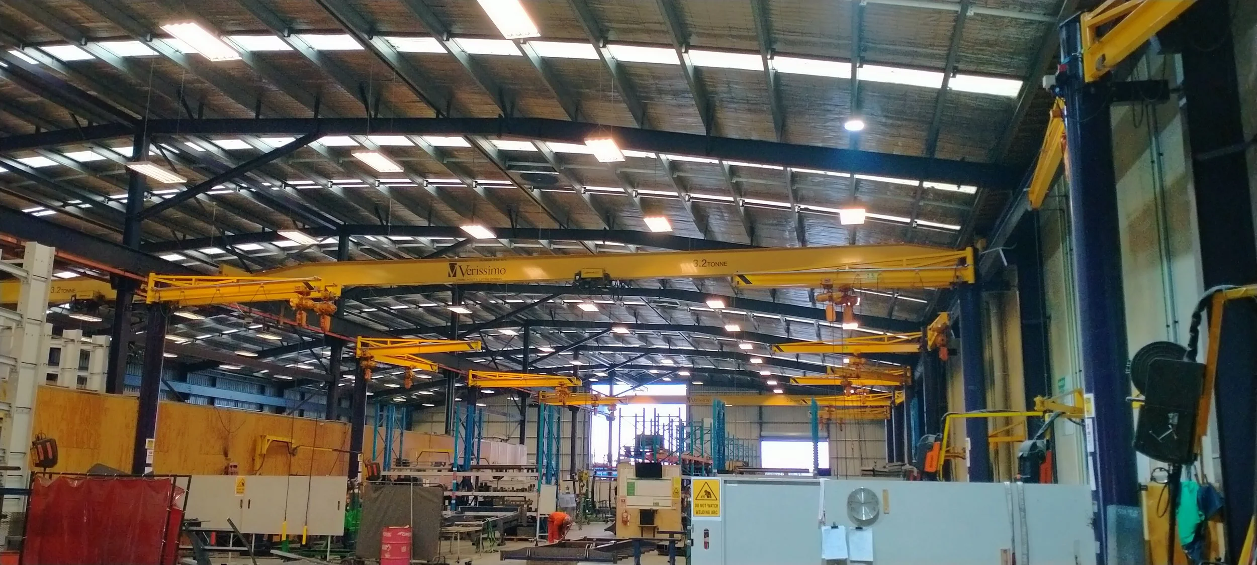 Inside a large industrial warehouse with multiple yellow overhead cranes and a high metal roof.