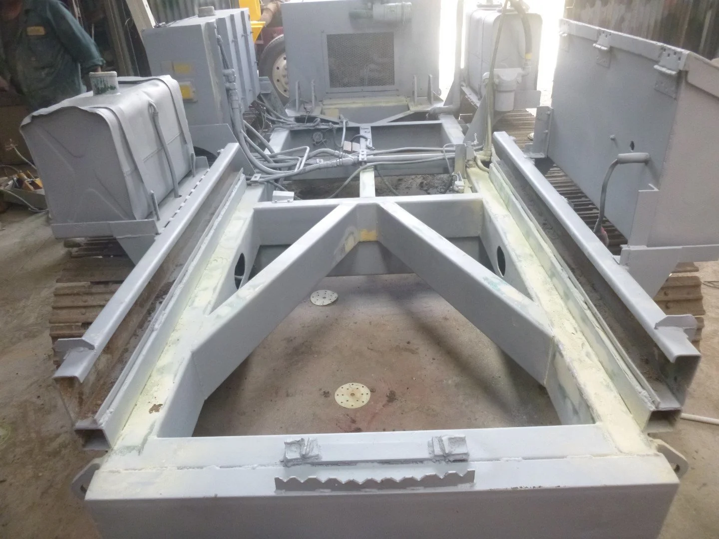 A partially assembled, EWP  frame with tracks, hydraulic cables, and structural components, in a workshop or garage setting.