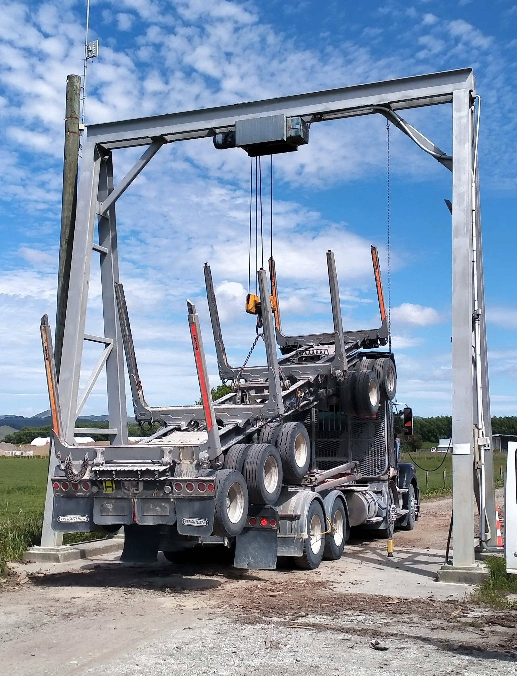 A log truck with its trailer being lifted by a crane onto the main truck body.