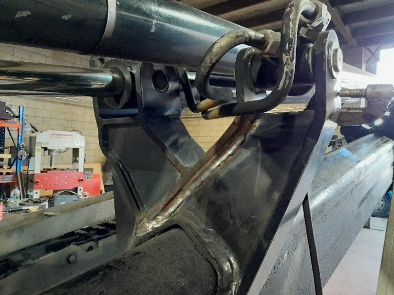 Close-up of industrial machinery parts including pipes, brackets, and metal welding, within a workshop setting. Crane boom repair
