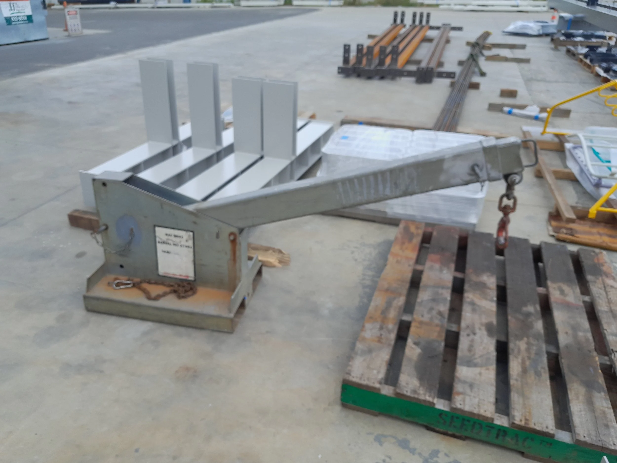 Construction site with metal cart filled with metal sheets, wooden pallets, and steel bars scattered on cement floor. Forklift jib attachment.