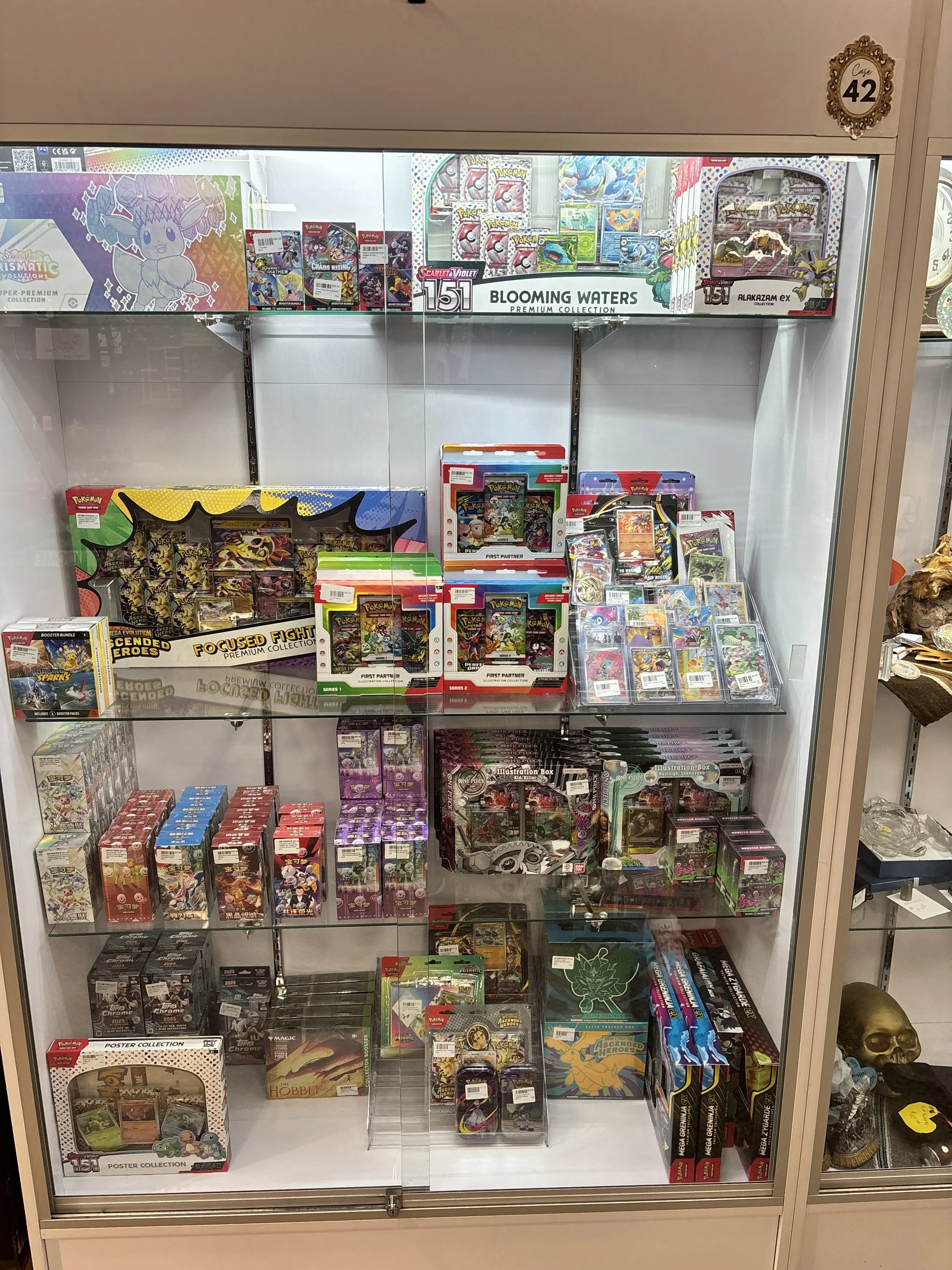 A display case filled with Pokémon merchandise including trading cards, card packs, collectibles, and boxes from various Pokémon collections.