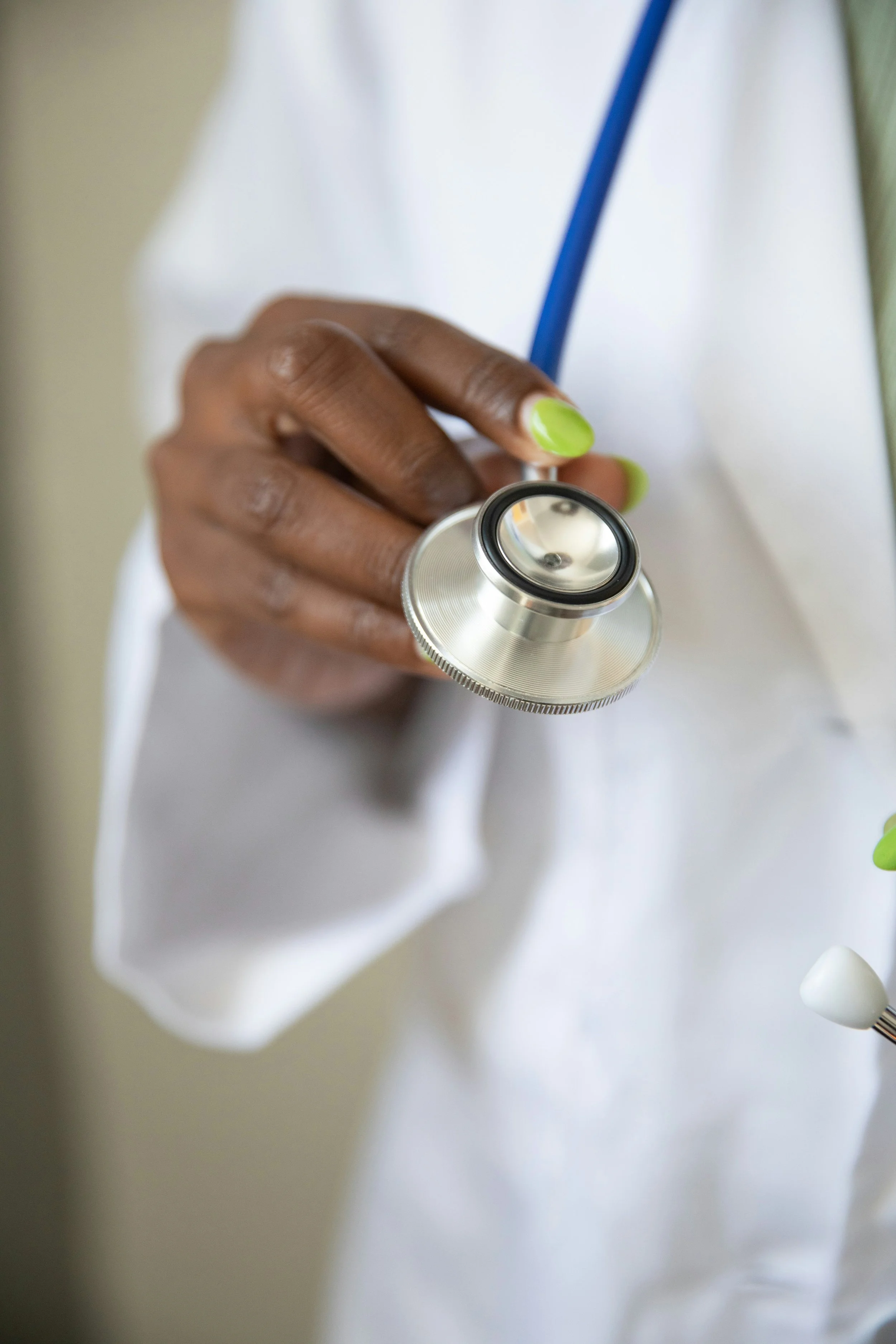 A person with green-painted nails holding a stethoscope, wearing a white coat or medical scrubs.