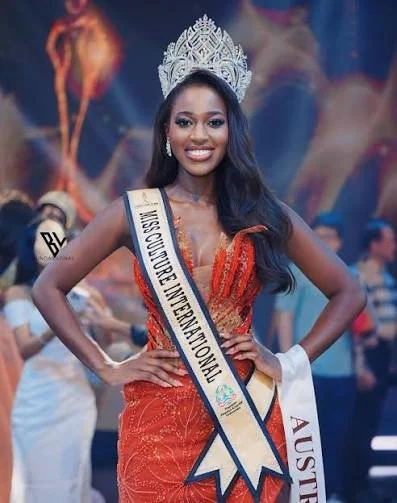 Ashleigh Gonde, Beauty pageant contestant wearing a crown and sash that reads 'Miss Globe International,' in a red dress with a blue background.