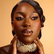 Close-up of a woman wearing makeup and a pearl choker necklace, with a warm beige background.