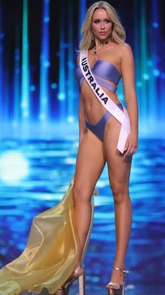 Zoe Creed pageant contestant representing Australia in a swimsuit with a sash, standing on stage with a blue and green illuminated background.