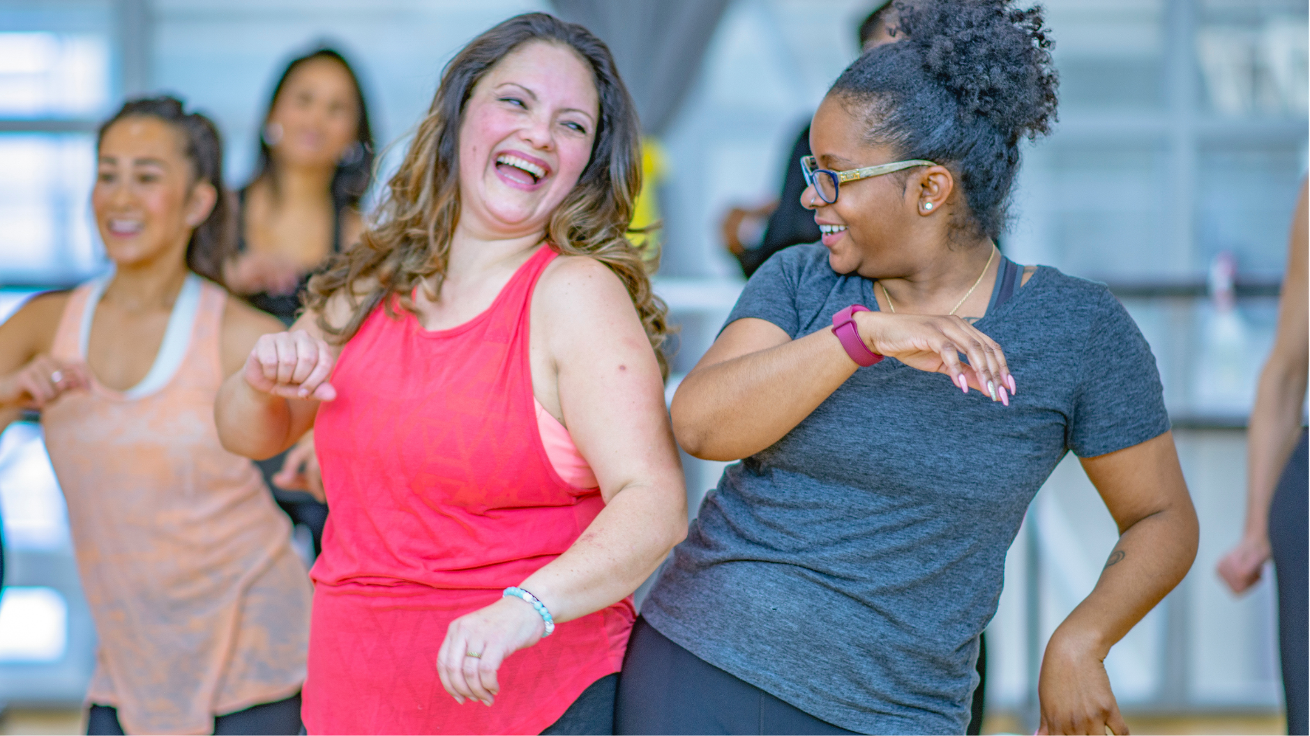 Group of women smiling and dancing at a fitness class, enjoying themselves.