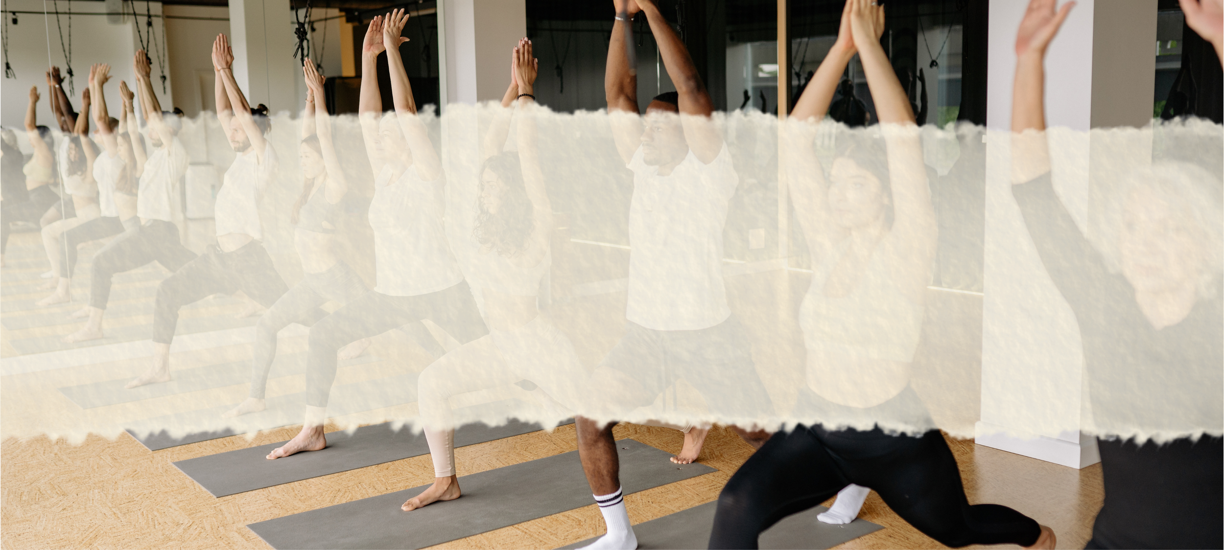 People participating in a yoga or meditation class, sitting on mats with eyes closed and hands raised above their heads, inside a well-lit room with mirrors.