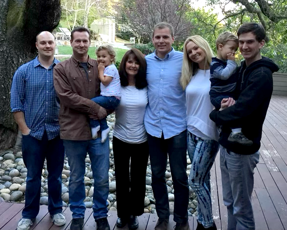 Pamela West and her framily standing outdoors on a wooden deck with trees in the background.