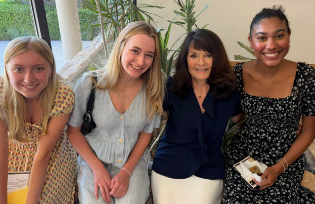 Pamela West and students smiling and posing together inside a building, with plants behind them.