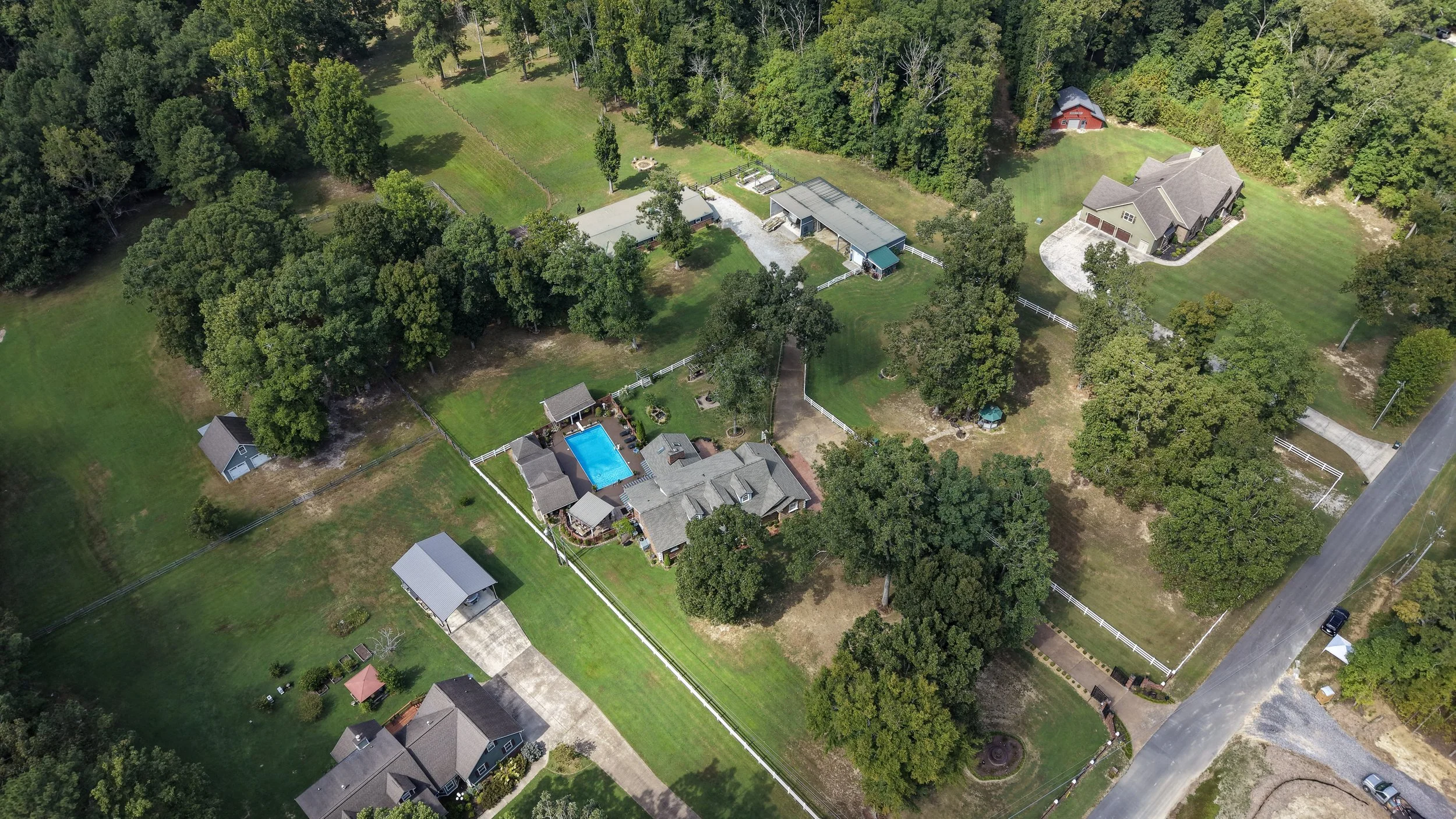 An aerial view of a residential area with multiple houses, a swimming pool, and a lot of green trees and lawns.