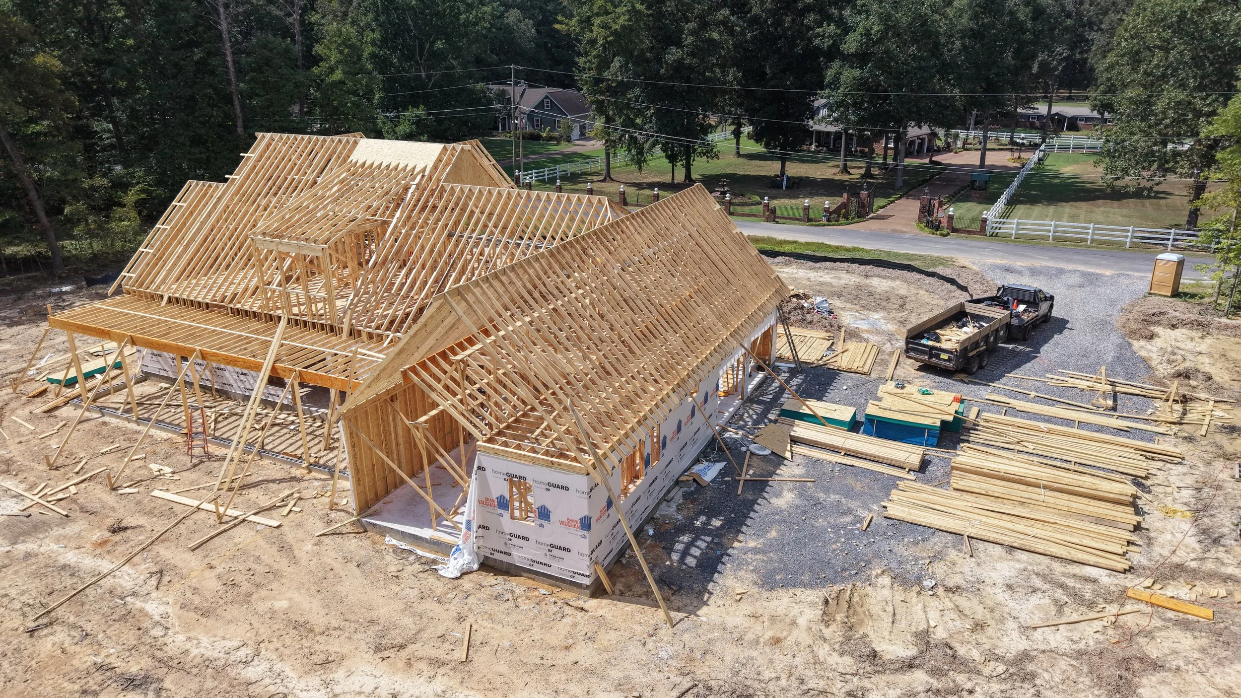 Construction site with a wooden house frame being built, surrounded by construction materials and a truck.